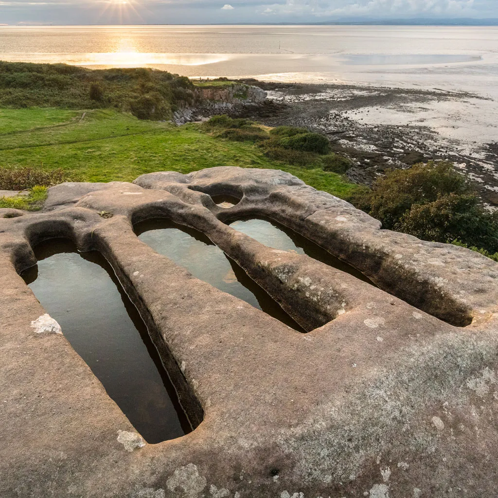 three tombs carved out of a flat rock by the sea