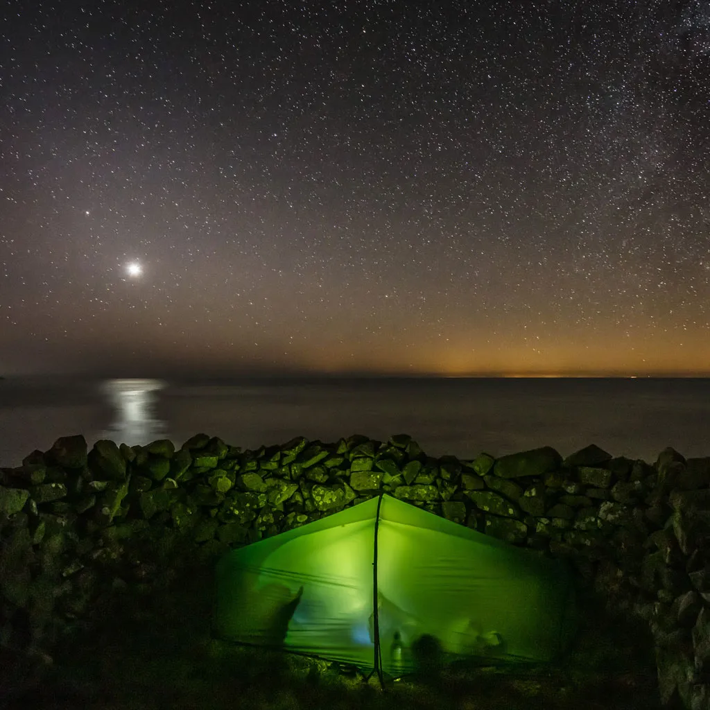 A green tent by the sea at night illuminated from within