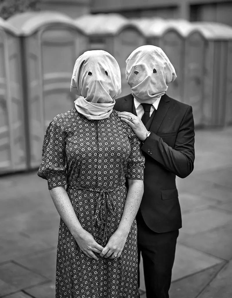 portrait of two people with white sacks over their heads with eye holes