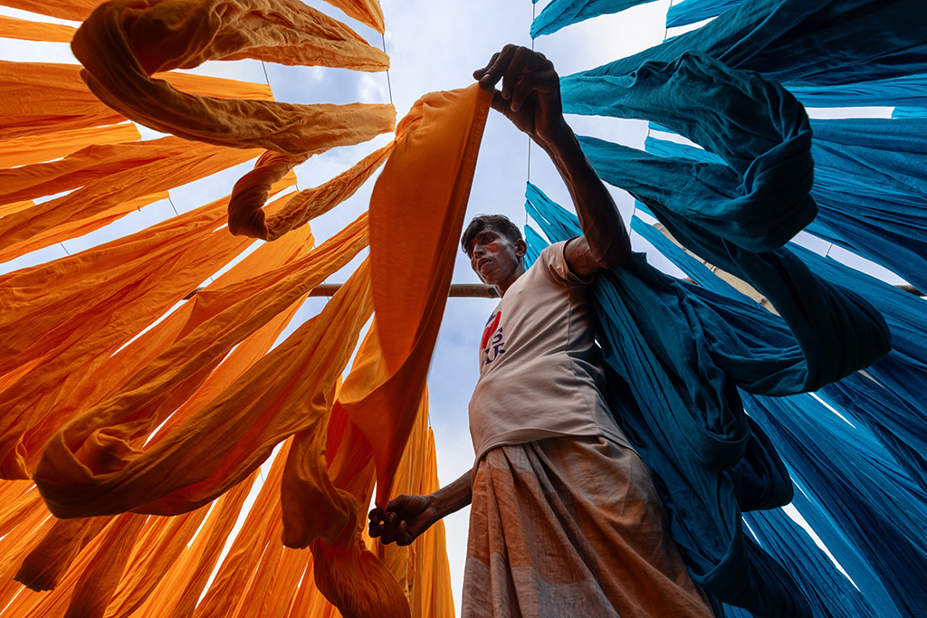 a textile worker in Narayanganj, Bangladesh, carefully arranging freshly dyed fabrics on wooden frames