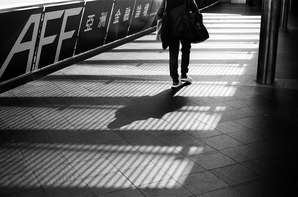 street photo of someone walking along a bridge in between shadows